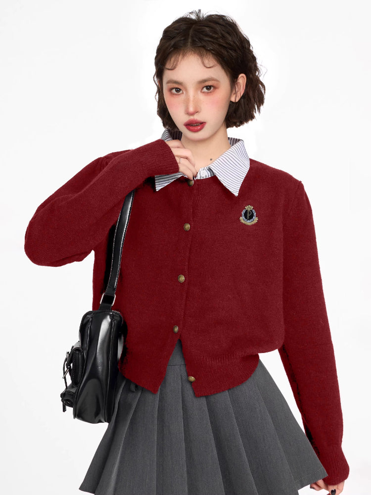 Woman wearing a burgundy knit cardigan with a collared neckline and button-up front, paired with a grey pleated skirt.