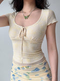 Front view of a woman wearing a fitted yellow sheer top with a floral design and short sleeves.