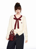 Woman holding a burgundy handbag while wearing a cream knit cardigan