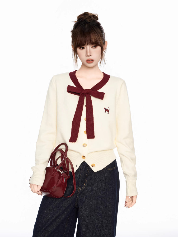 Woman holding a burgundy handbag while wearing a cream knit cardigan