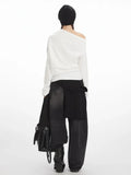 Back view of a woman wearing a white long-sleeve graphic print top with an off-the-shoulder design and black jeans.