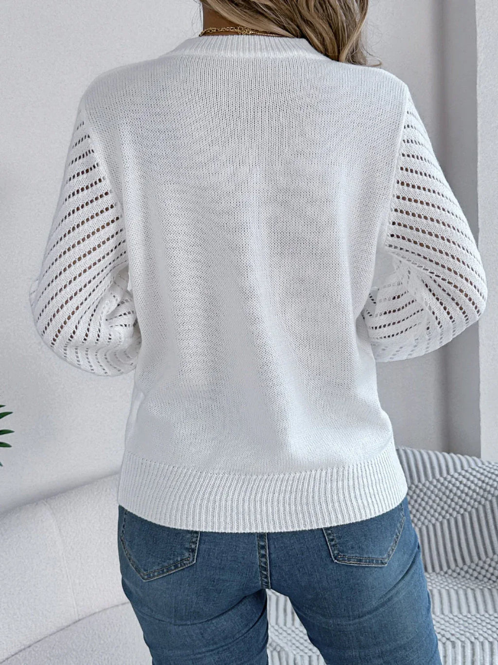 Back view of a woman wearing a white knit sweater with openwork sleeve details.