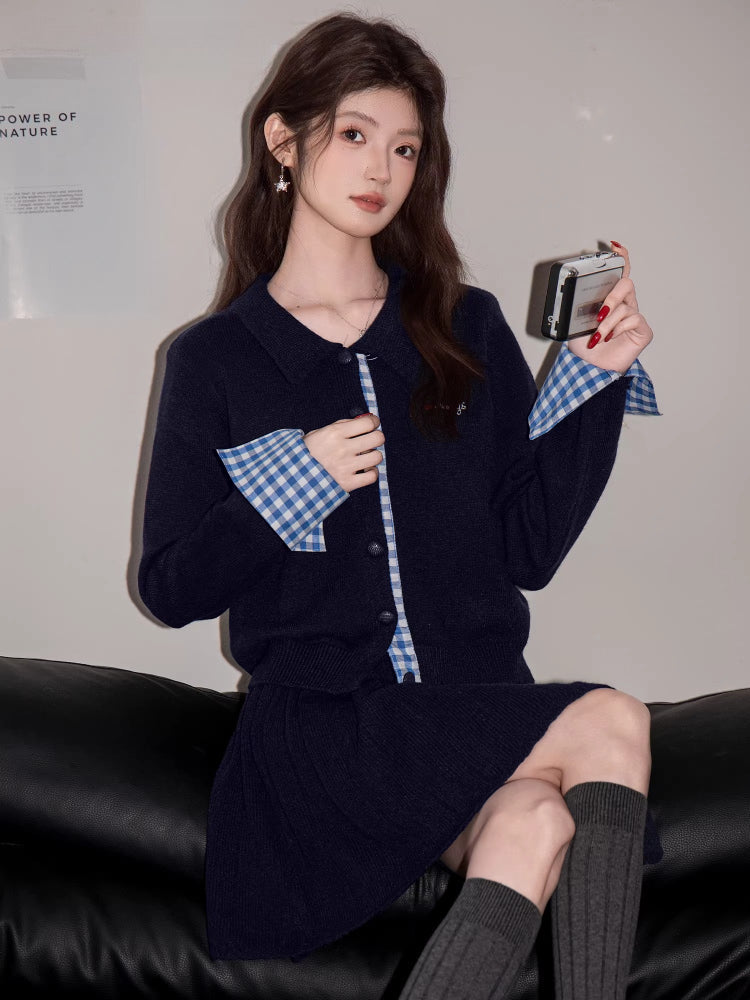 Close-up of a woman in a navy knit cardigan with blue gingham cuffs, holding a small silver camera.