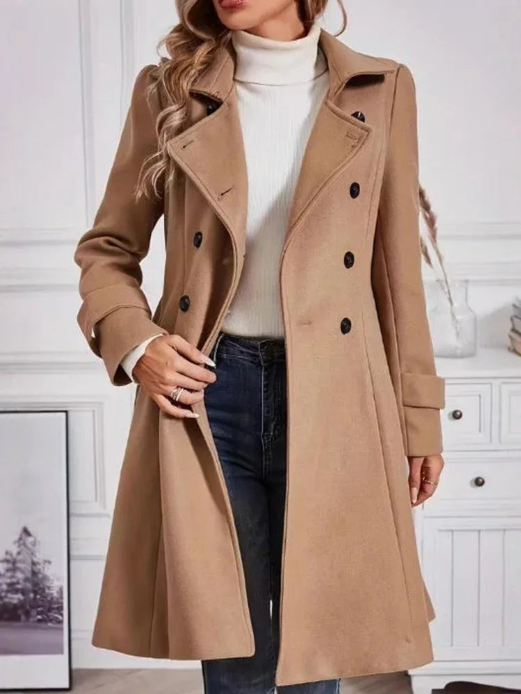 Woman wearing a camel double-breasted wool blend coat, open to show a white turtleneck and blue jeans