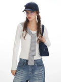 Close-up of a woman wearing a white long-sleeve top with a striped collar and blue wide-leg jeans, holding a navy handbag.