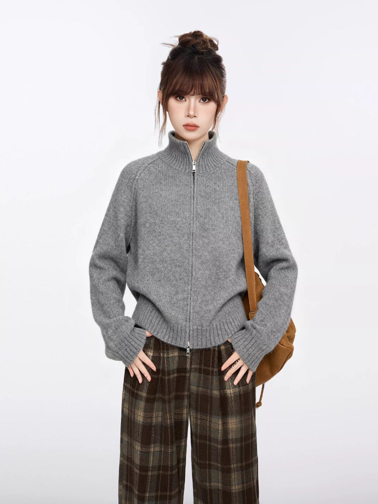 Woman wearing a grey zip-up knit sweater with a high neckline, standing with hands on hips