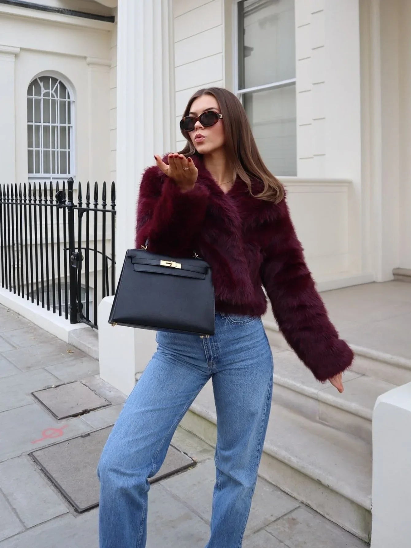 Woman wearing a burgundy faux fur jacket and blue jeans outdoors. Main image
