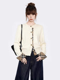 Close-up of a cream knit cardigan with plaid detailing on the placket and cuffs.