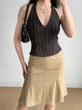 Woman wearing a dark patterned halter top and a tan skirt, holding a black handbag.