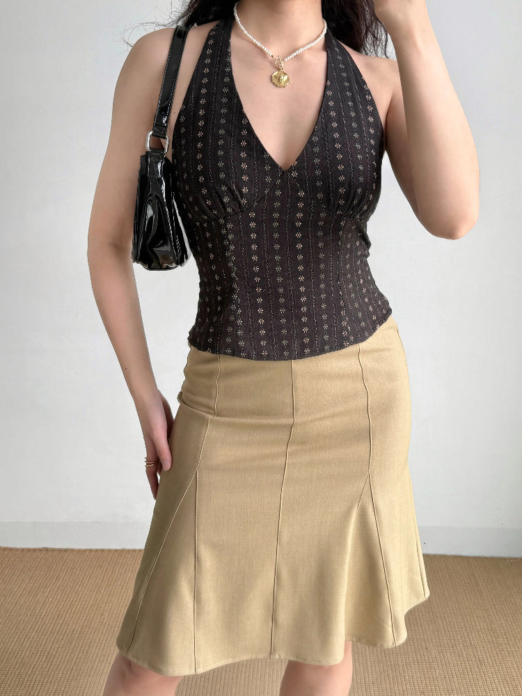 Woman wearing a dark patterned halter top and a tan skirt, holding a black handbag.