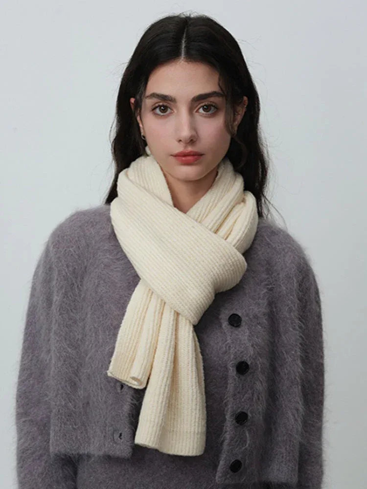 Woman with dark hair wearing a cream-colored ribbed knit scarf and a grey fuzzy cardigan