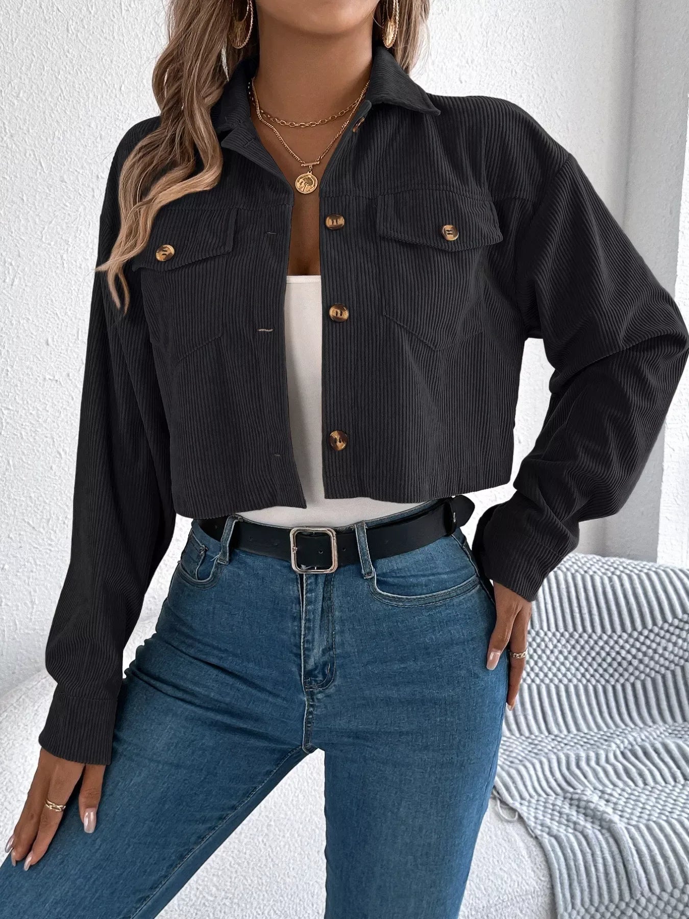 Front view of a woman in a black cropped corduroy jacket, white tank top, and blue jeans