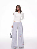 Woman in a white long-sleeve collared top and grey wide-leg sweatpants with colorful embellishments.