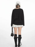 Back view of a woman wearing a black long-sleeved t-shirt with a graphic print, white polka dot skirt, black knee-high socks, and black boots.