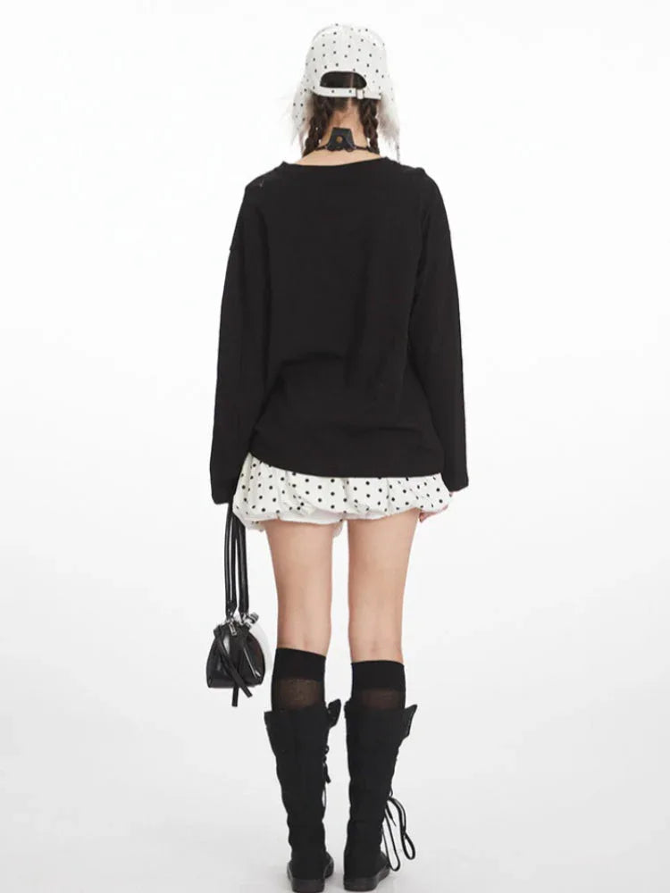 Back view of a woman wearing a black long-sleeved t-shirt with a graphic print, white polka dot skirt, black knee-high socks, and black boots.