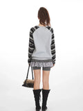 Back view of a model in a grey graphic print sweatshirt with striped sleeves and shorts.