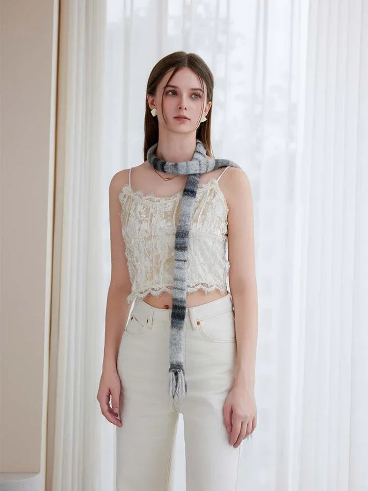 Full body shot of a woman in a white camisole and cream pants, with a long, striped knit scarf featuring tassels.
