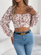 Model posing in a white floral print cropped top with blue denim jeans.