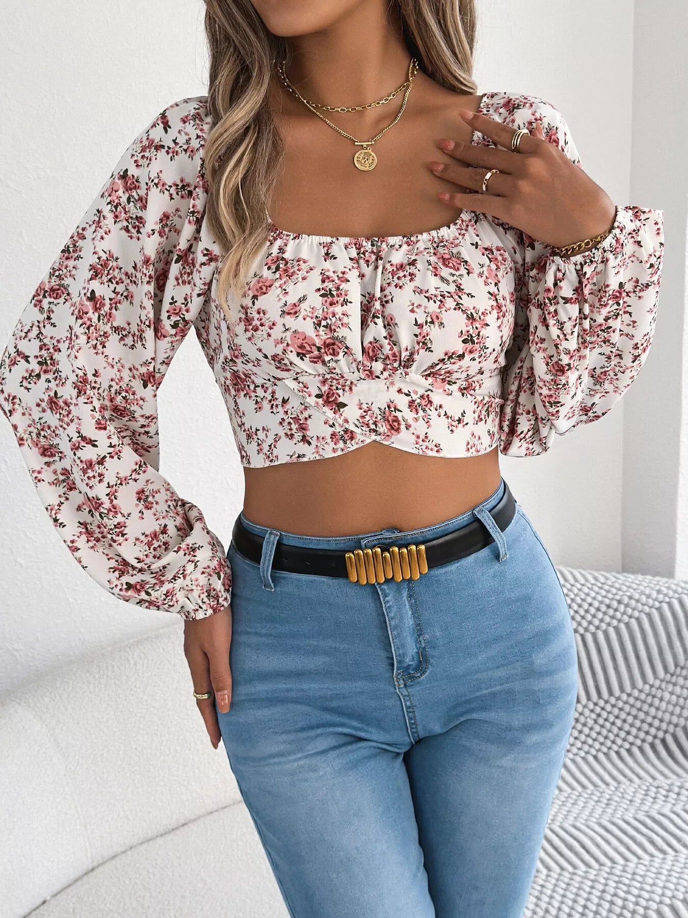 Model posing in a white floral print cropped top with blue denim jeans.