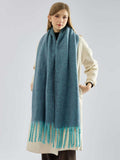 Full body shot of a woman in a cream coat accessorized with a teal oversized scarf.