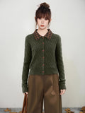 Woman wearing a dark green cable knit cardigan with a brown plaid collar and brown buttons.