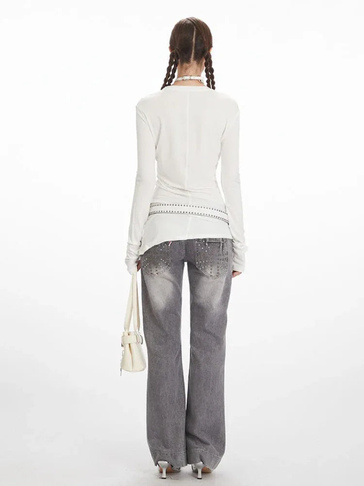 Model wearing a white long sleeve top with asymmetrical seam detail and grey jeans.