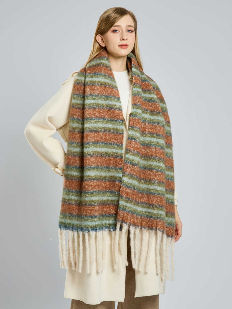 Woman wearing a long, wide scarf with horizontal stripes in rust, light blue, and green, featuring cream fringe at the ends.