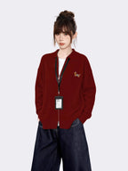 Woman wearing a red knit zip-up jacket with a collared neckline and embroidered graphic on the left chest.