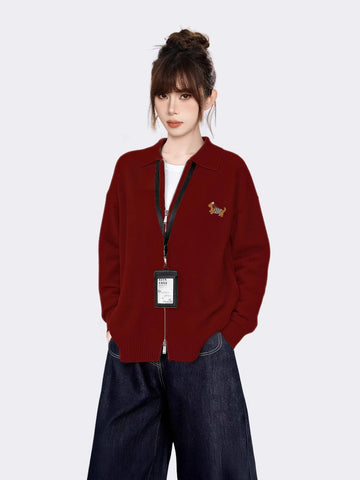 Woman wearing a red knit zip-up jacket with a collared neckline and embroidered graphic on the left chest.