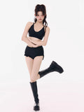Woman wearing a black halter bikini top and black ruffled hem shorts, with black platform boots.