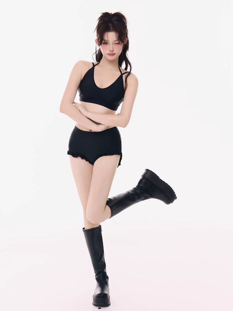 Woman wearing a black halter bikini top and black ruffled hem shorts, with black platform boots.