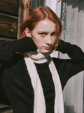 Woman posing with hands near her face, wearing a cream scarf and black sweater.