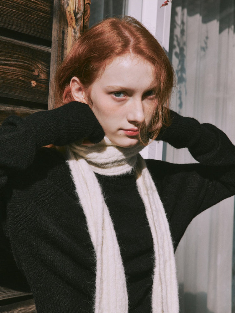 Woman posing with hands near her face, wearing a cream scarf and black sweater.