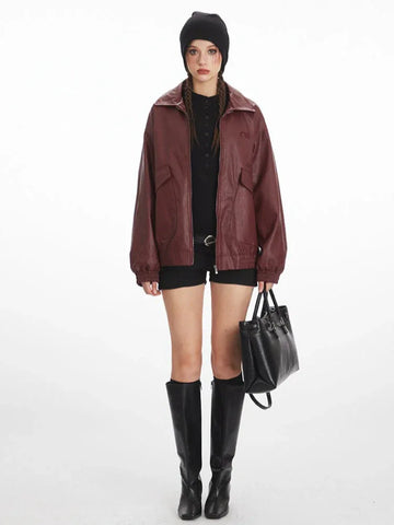 Woman wearing a burgundy faux leather bomber jacket with a black beanie and black shorts