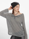 woman touching her hair while wearing a black and white striped long-sleeve shirt with a wide collar