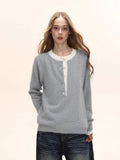 Woman wearing a light grey long-sleeved knit sweater with a white contrast neckline and button-up placket, paired with distressed denim jeans.