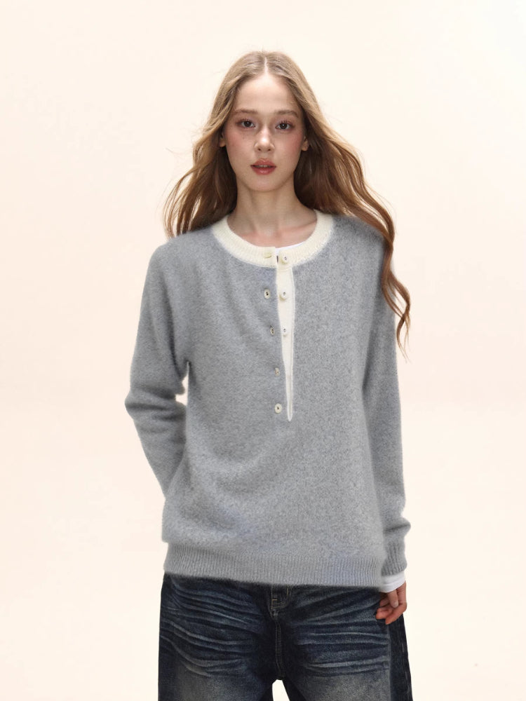 Woman wearing a light grey long-sleeved knit sweater with a white contrast neckline and button-up placket, paired with distressed denim jeans.