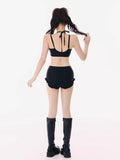 Back view of a woman wearing a black halter bikini top and black ruffled hem shorts, with black platform boots.