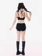 Back view of a woman wearing a black halter bikini top and black ruffled hem shorts, with black platform boots.