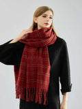 Woman adjusting a red plaid scarf with fringe detailing.