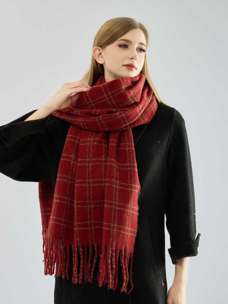 Woman adjusting a red plaid scarf with fringe detailing.