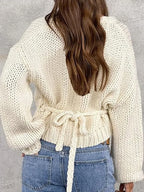Back view of a woman in a cream chunky knit wrap sweater with a tie waist.