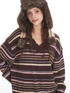 Close-up of a woman wearing a brown striped knit sweater with a v-neck and collar detail, and a brown faux fur hat with ear flaps.