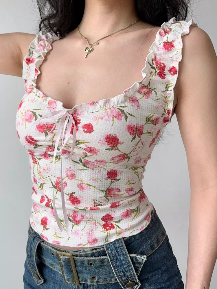 Side view of a woman wearing a white floral print top with ruffled off-the-shoulder cap sleeves and a sweetheart neckline with a pink ribbon tie, paired with denim.