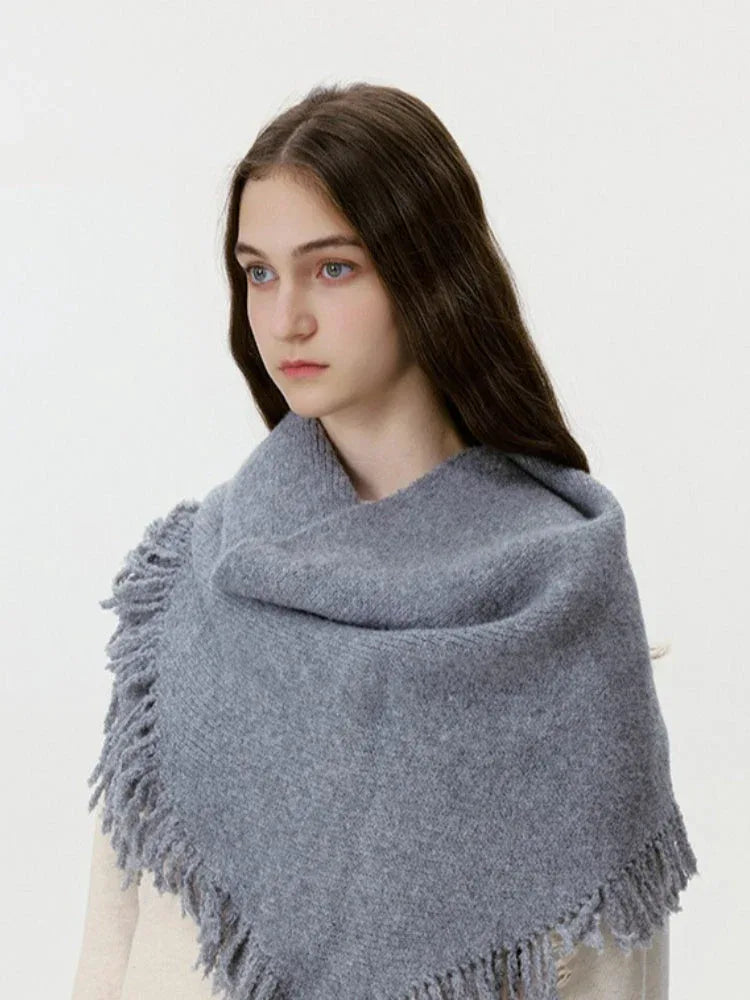 Close-up of a woman wearing a grey knit scarf with fringe detail over a cream sweater.