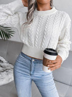 Woman holding a coffee cup while wearing a white cropped cable knit sweater and light wash jeans