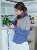 Close-up of a woman's hands holding a bottle of green beverage while wearing a layered outfit and a multi-colored scarf.