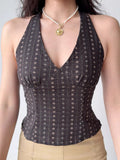 Woman wearing a dark patterned halter top with a v-neckline and a pearl necklace.