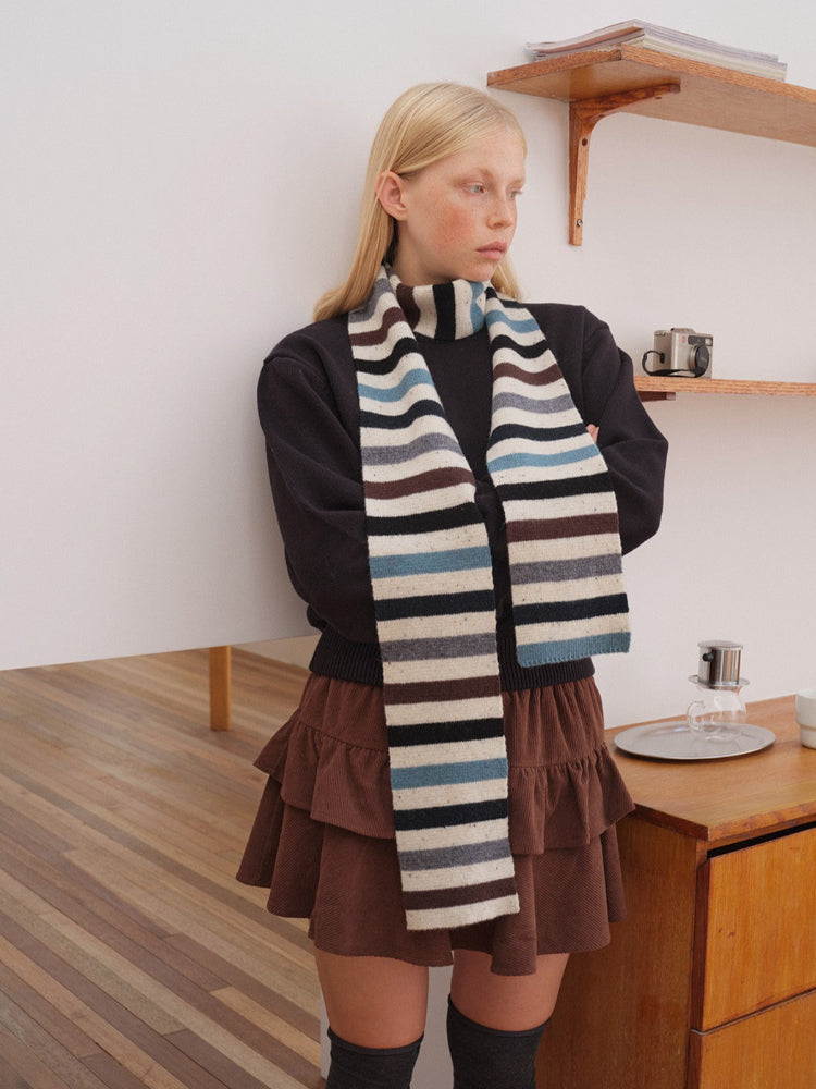 Woman wearing a striped knitted scarf with black, white, blue, and brown horizontal stripes
