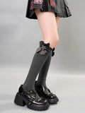 A person wearing gray knee-high socks with a gray flower embellishment and bow detail, paired with platform shoes.